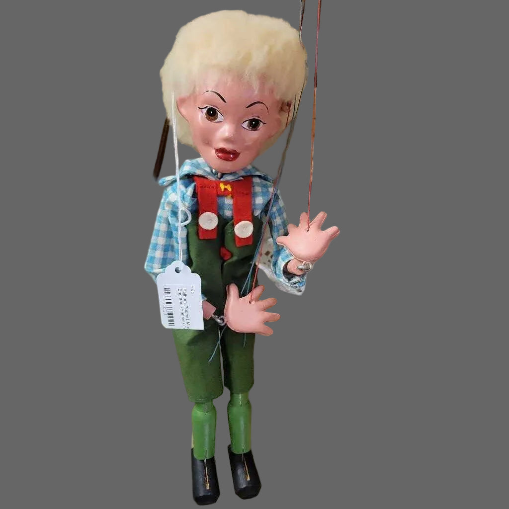 Vintage-style puppet with blonde wig and red suspenders, standing next to a wicker basket.