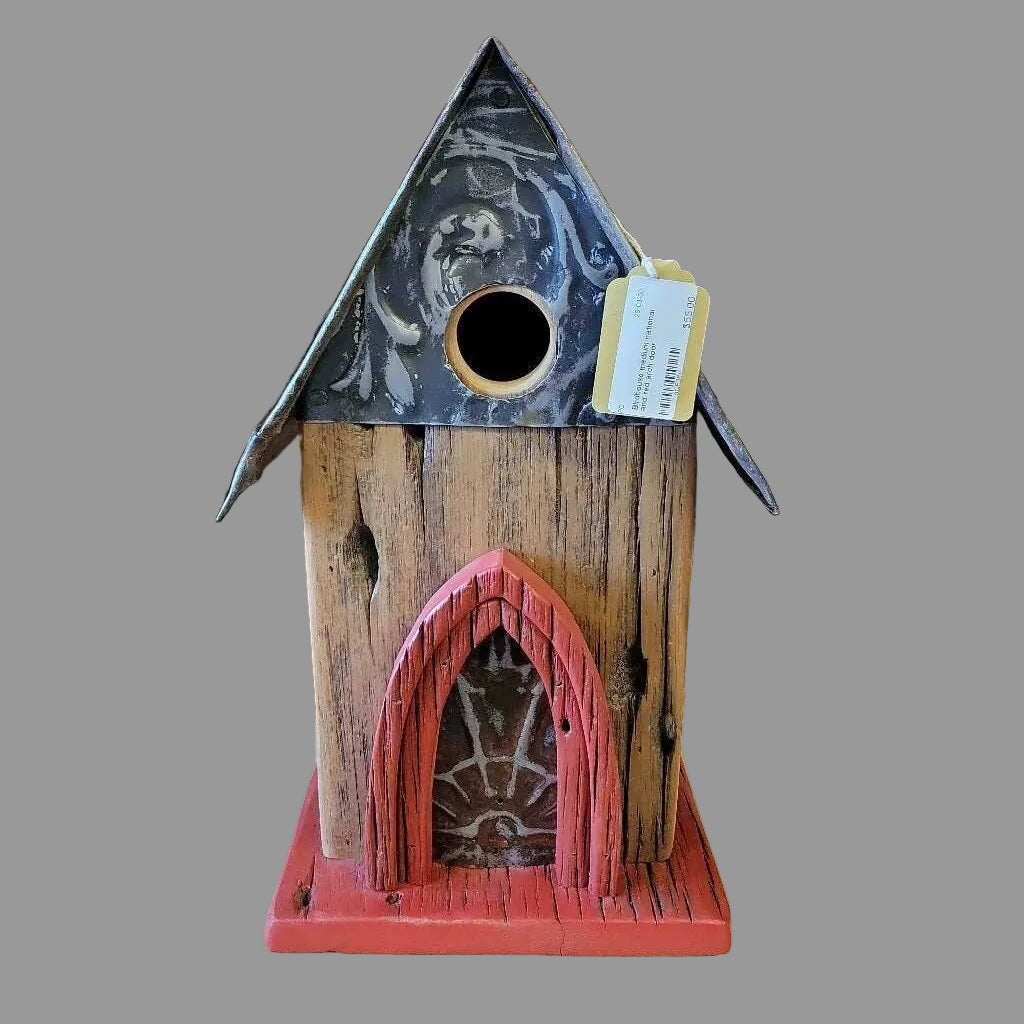 Wooden birdhouse with a red base and black roof on a wooden surface.